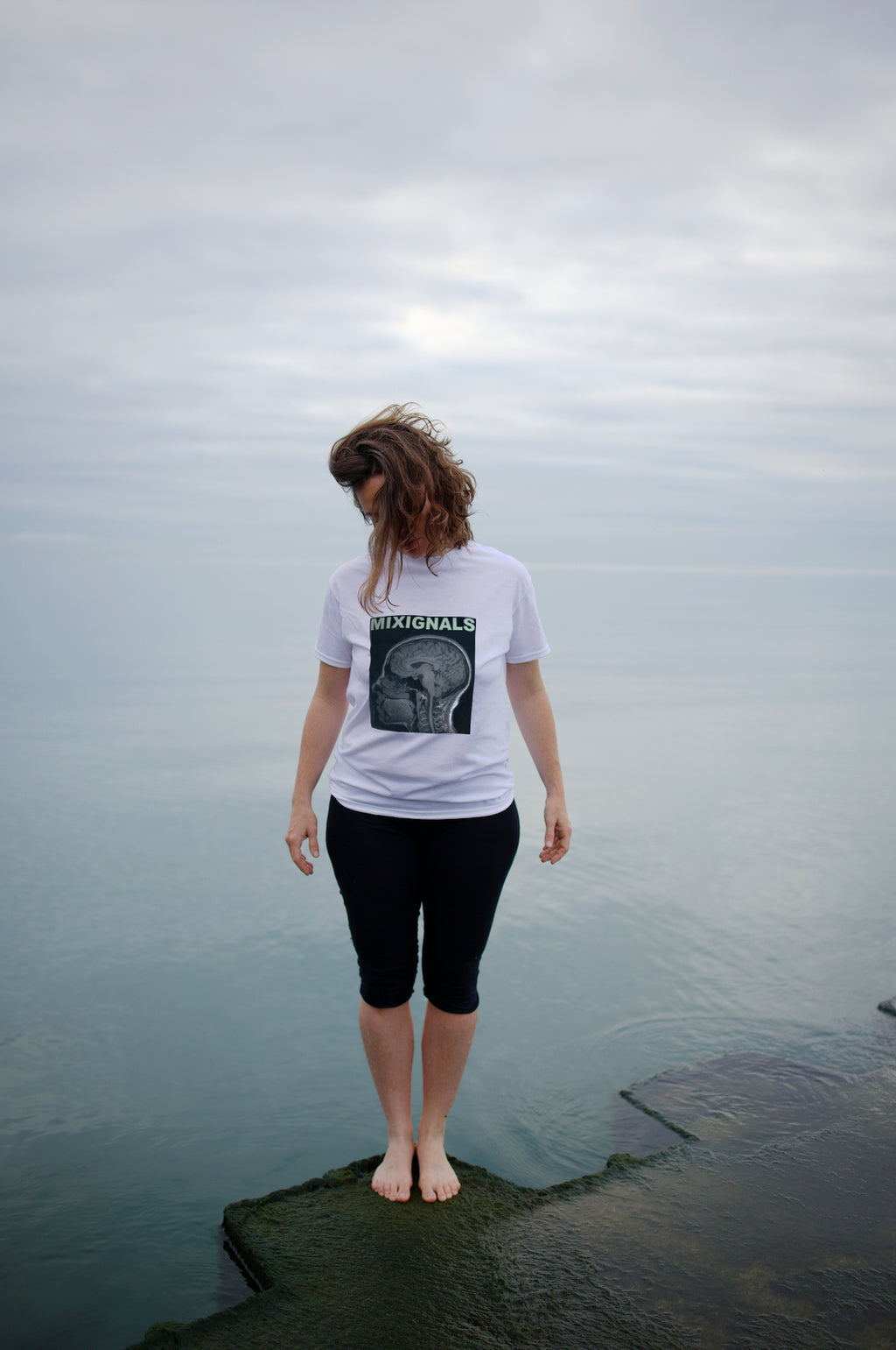 MIXMON – woman by the water, seen from behind, wearing the colour-inverted BRAIN SCAN design on a white tee (inverted version, not yet for sale) – MIXIGNALS by Alex Beriault