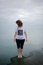 MIXMON – woman by the water, seen from behind, wearing the colour-inverted BRAIN SCAN design on a white tee (inverted version, not yet for sale) – MIXIGNALS by Alex Beriault